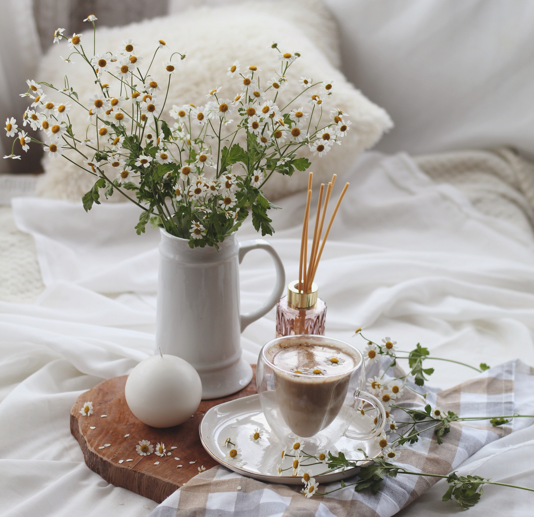 a vase of chamomile flowers beside a cup of chamomile tea