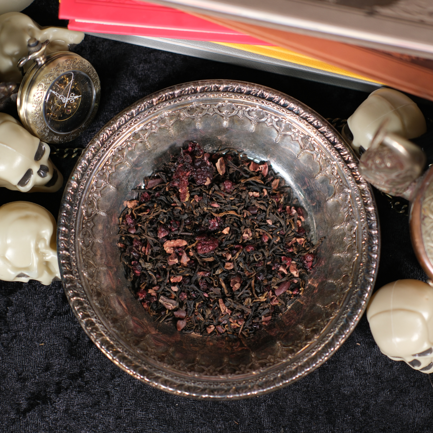 Silver bowl with dried herbs on a dark surface with decorative items.