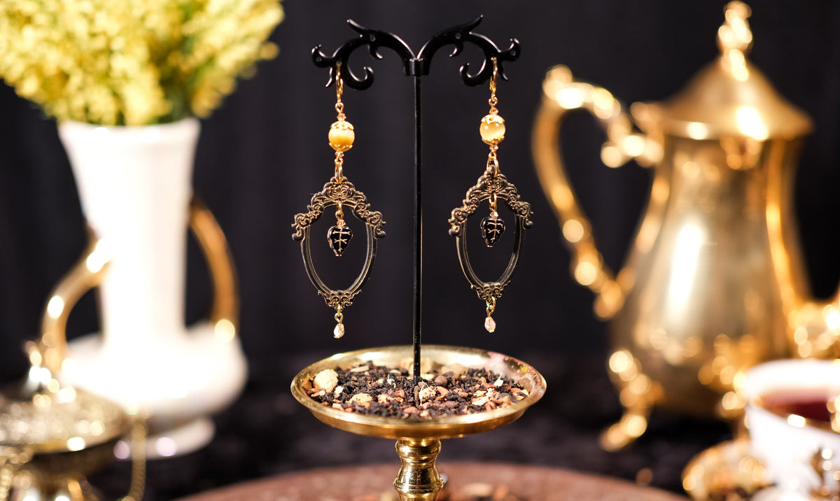 Ornate gold earrings on a stand with a blurred background of decorative items.