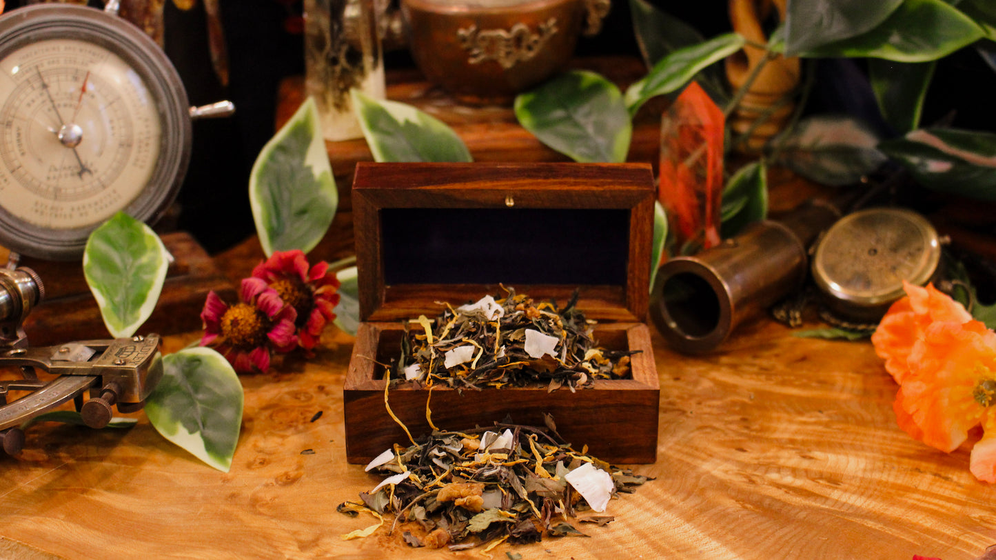Wooden box with blended tea spilling out on a burl wood surface with plants, vintage navigation tools, and other eclectic props