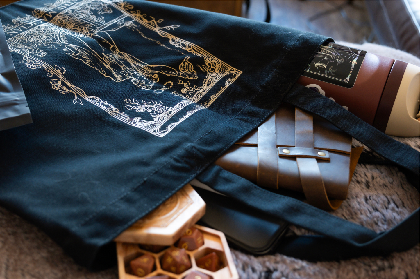 Black canvas bag with gold screen printing of a teafling in the pose of a Magician Tarot card, pouring tea