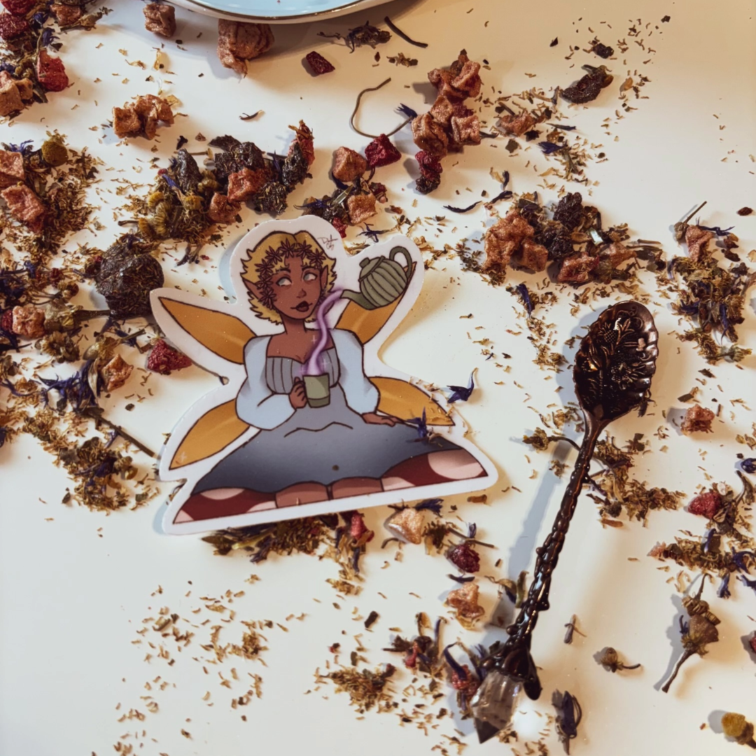 Sticker of a fairy with a tea pot surrounded by dried herbs and flowers on a white surface.