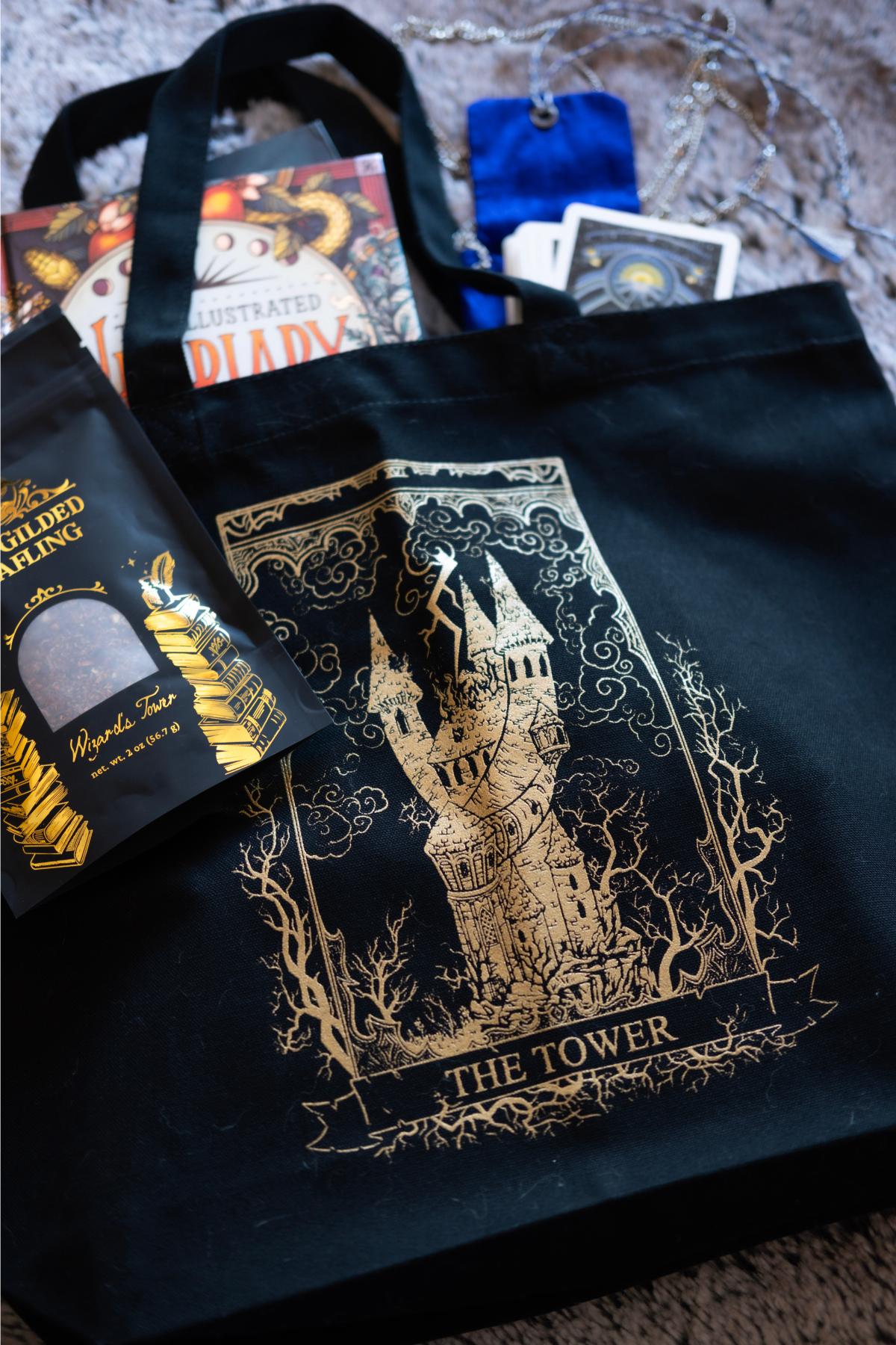 Black tote bag with 'The Tower' design, surrounded by books and cards on a textured surface.